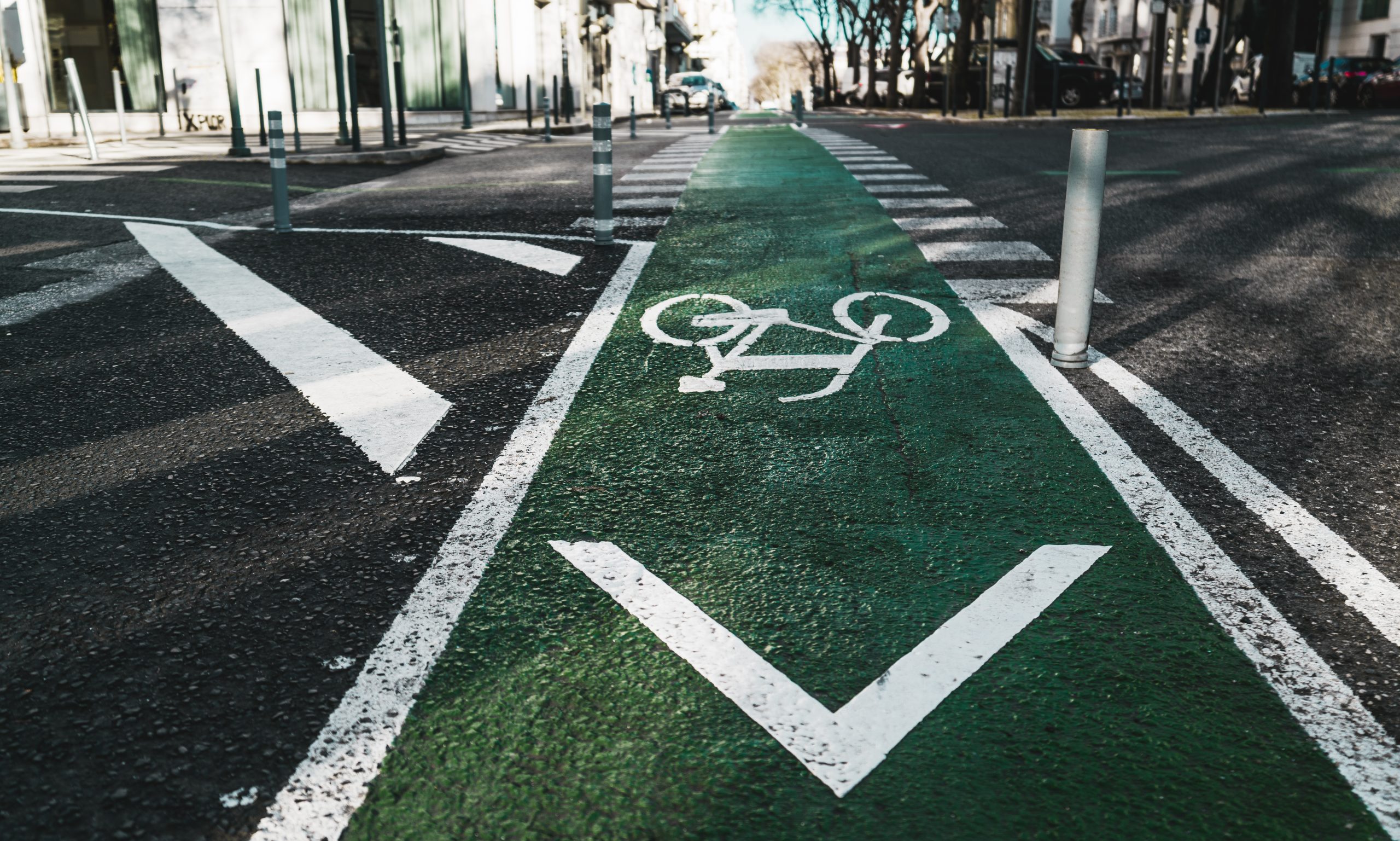 Urban wide-angle view of a modern city road in Lisbon with bicycle marking on green asphalt and two lanes of opposite directions, a pedestrian crossing in the distance, plastic posts in the foreground